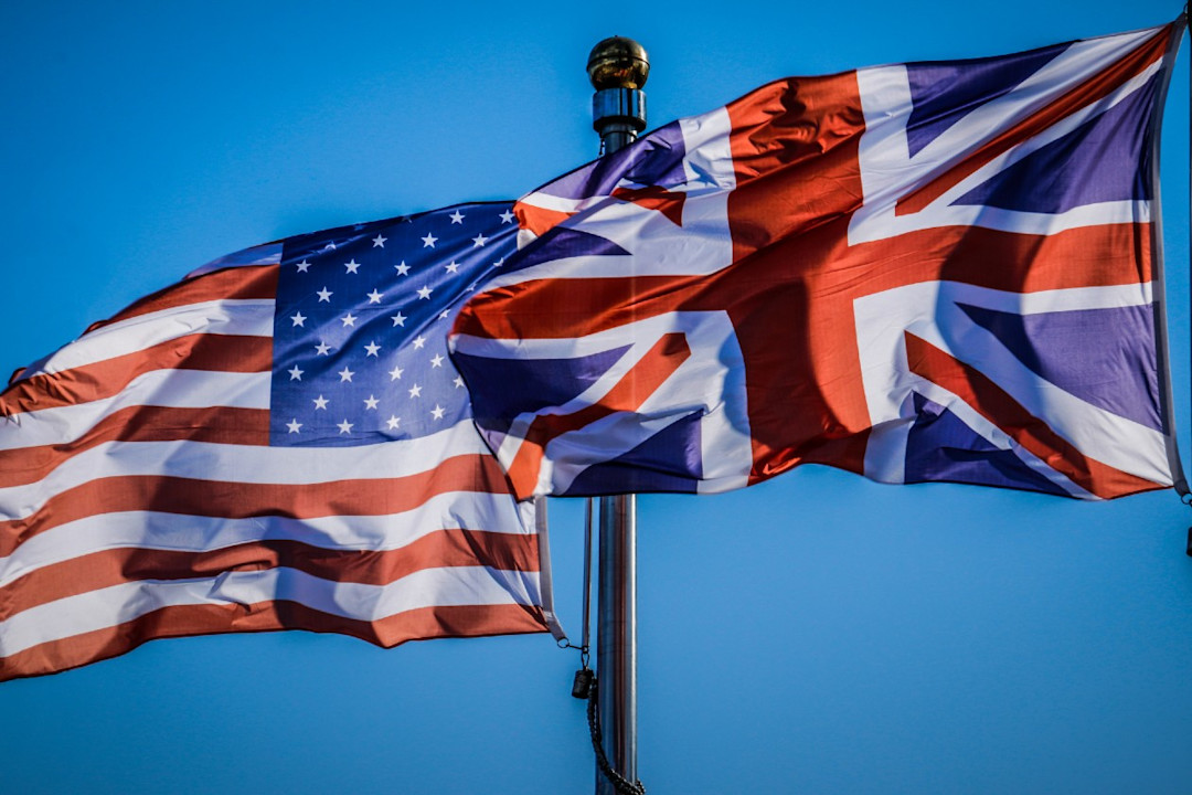 US and UK flags flying next to eachother against a blue skyline.jpg